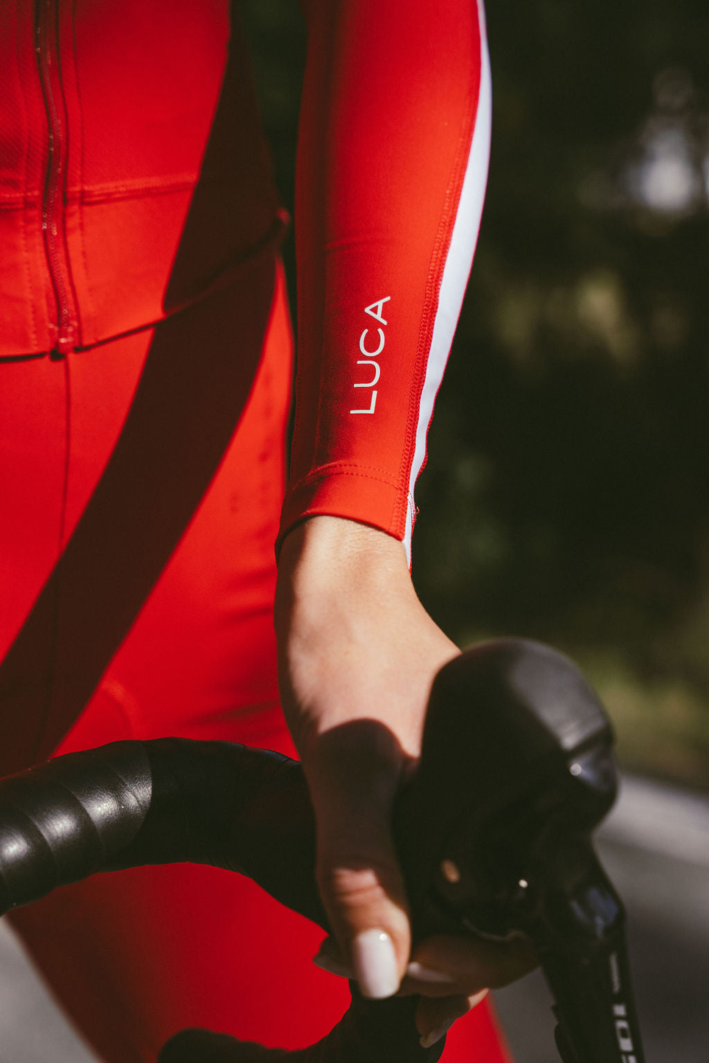 Close-up-of-a-red-cycling-dress- sleeve-with-LUCA-personalization- written-in-white-showing-a-cyclist- gripping-handlebars