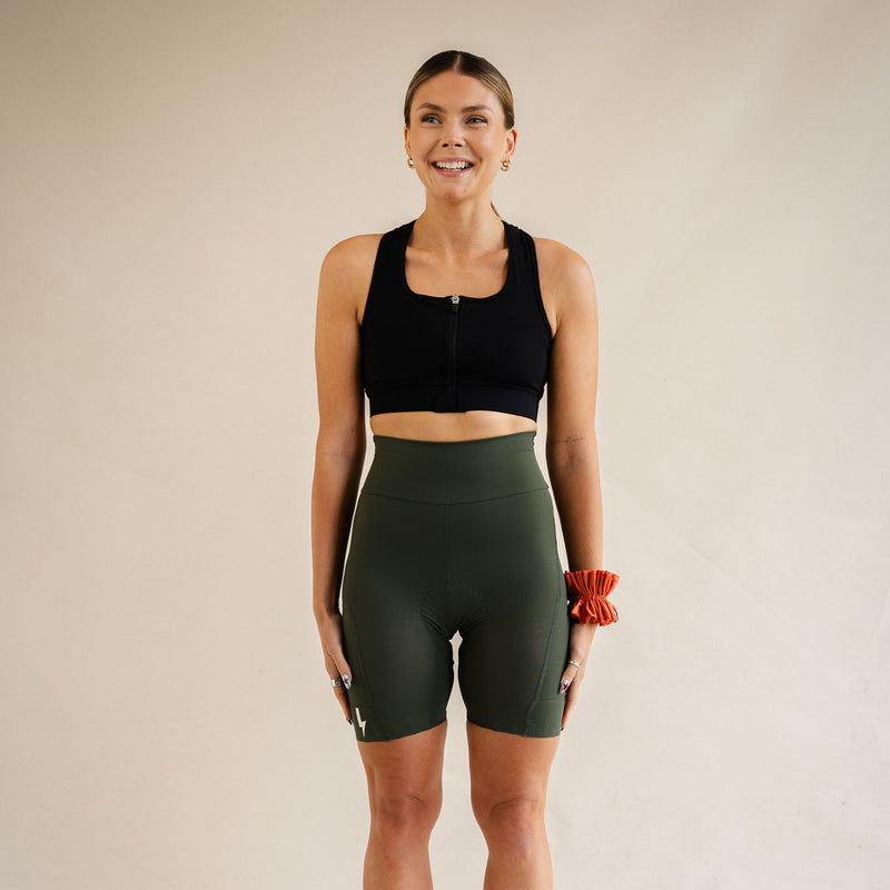 A-smiling-woman-looking-to-the-side- modeling-a-black-front-zip-sport-bra- and high-waisted-olive-green-biker- shorts-by-LUCA