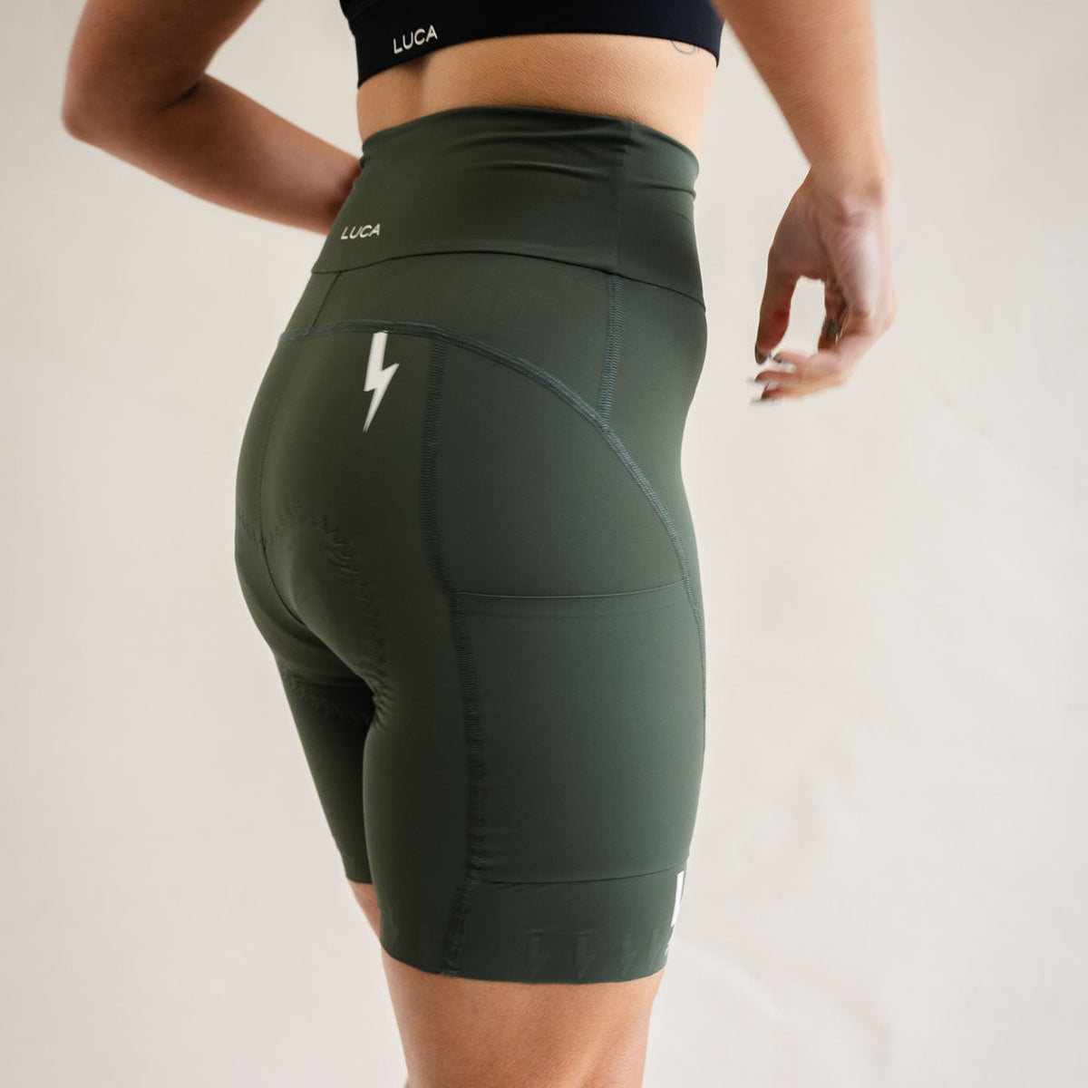 Close-up-side-view-of-a-woman- wearing-LUCA-high-waisted-olive- green-biker-shorts-showing-the-side- pocket-and-white-lightning-bolt-logo