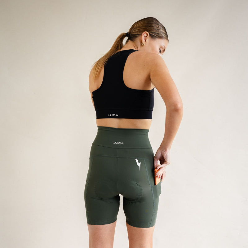 A-smiling-woman-looking-to-the-side- modeling-a-black-front-zip-sport-bra- and high-waisted-olive-green-biker- shorts-by-LUCA