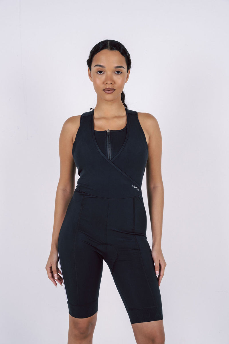 Back-view-of-a-woman-on-a-bicycle-wearing-black-cycling-Road- All-In-One-with-white-stripe-paneling-along-the-back-and-sides- Features-a-padded-seat-and- racerback-design-for-competitive- biking