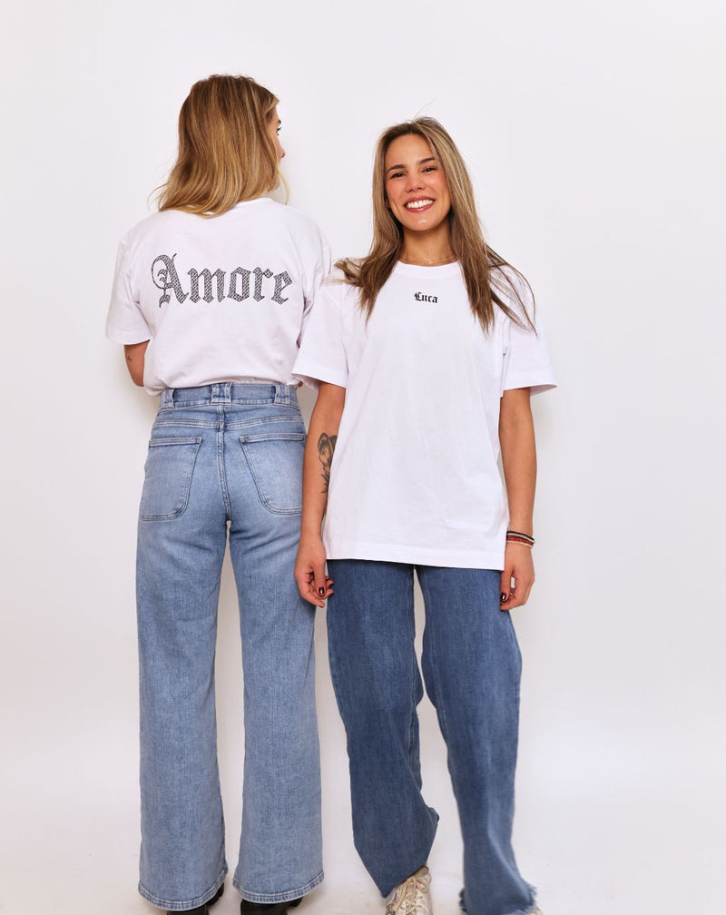 Front-view-of-a-woman-wearing-an- oversized-white-t-shirt-featuring-the-word-"Luca"-printed-in-a-small- black-gothic-font-on-the-chest-She- is-also-wearing-blue-jeans