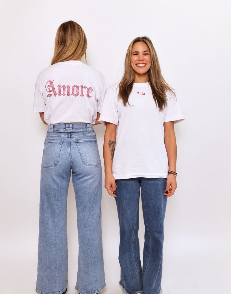 Smiling-model-wearing-a-white-Luca-logo-t-shirt-with-a-small-red- script-logo-and-wide-leg-denim-jeans