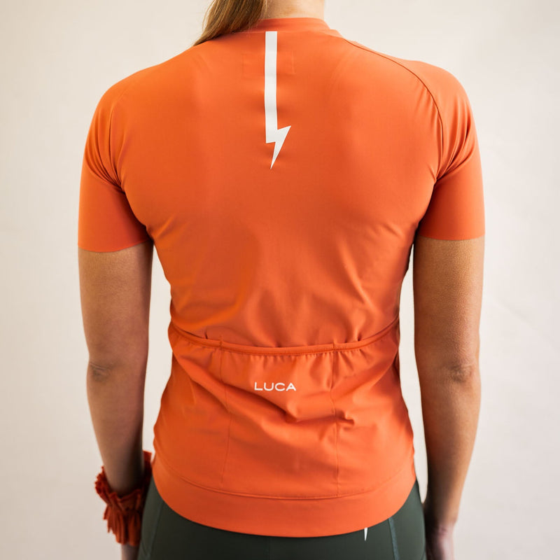Cyclist wearing LUCA Soleil jersey in aperol with cycling shorts, front view