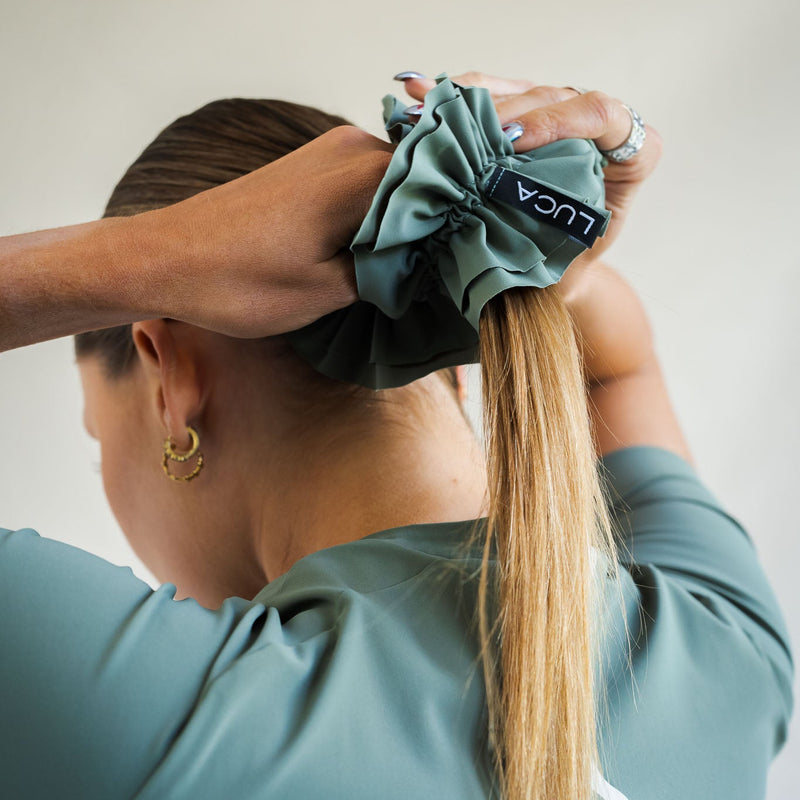 LUCA Uplift scrunchie in matcha worn on wrist next to cycling shorts